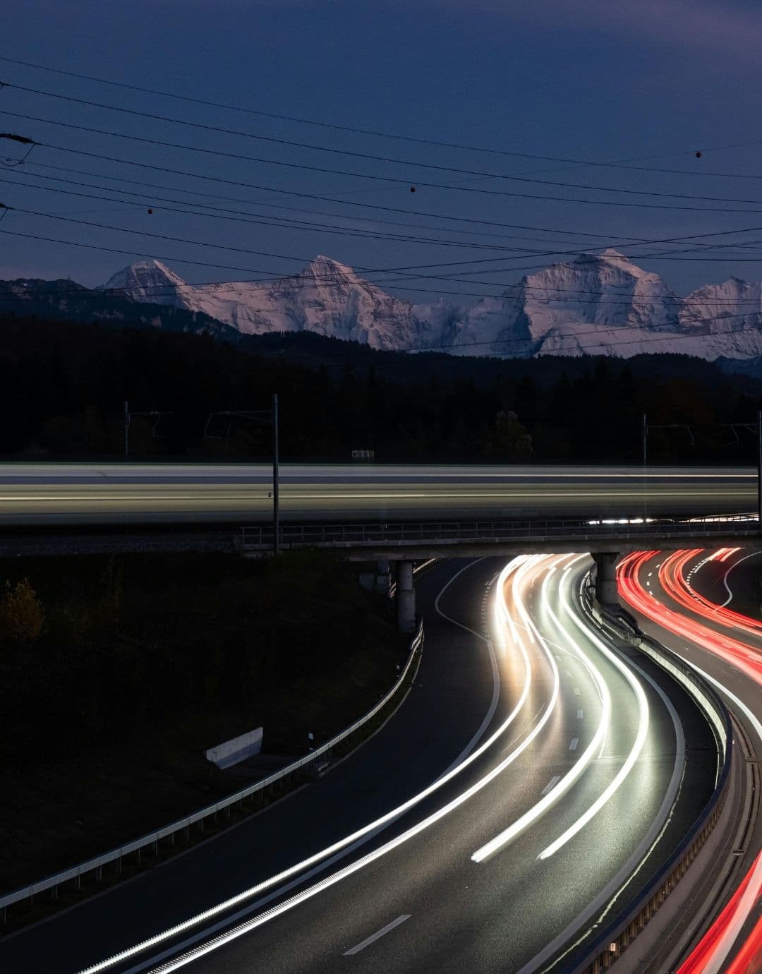 Autoroute suisse de nuit devant un massif alpin enneigé
